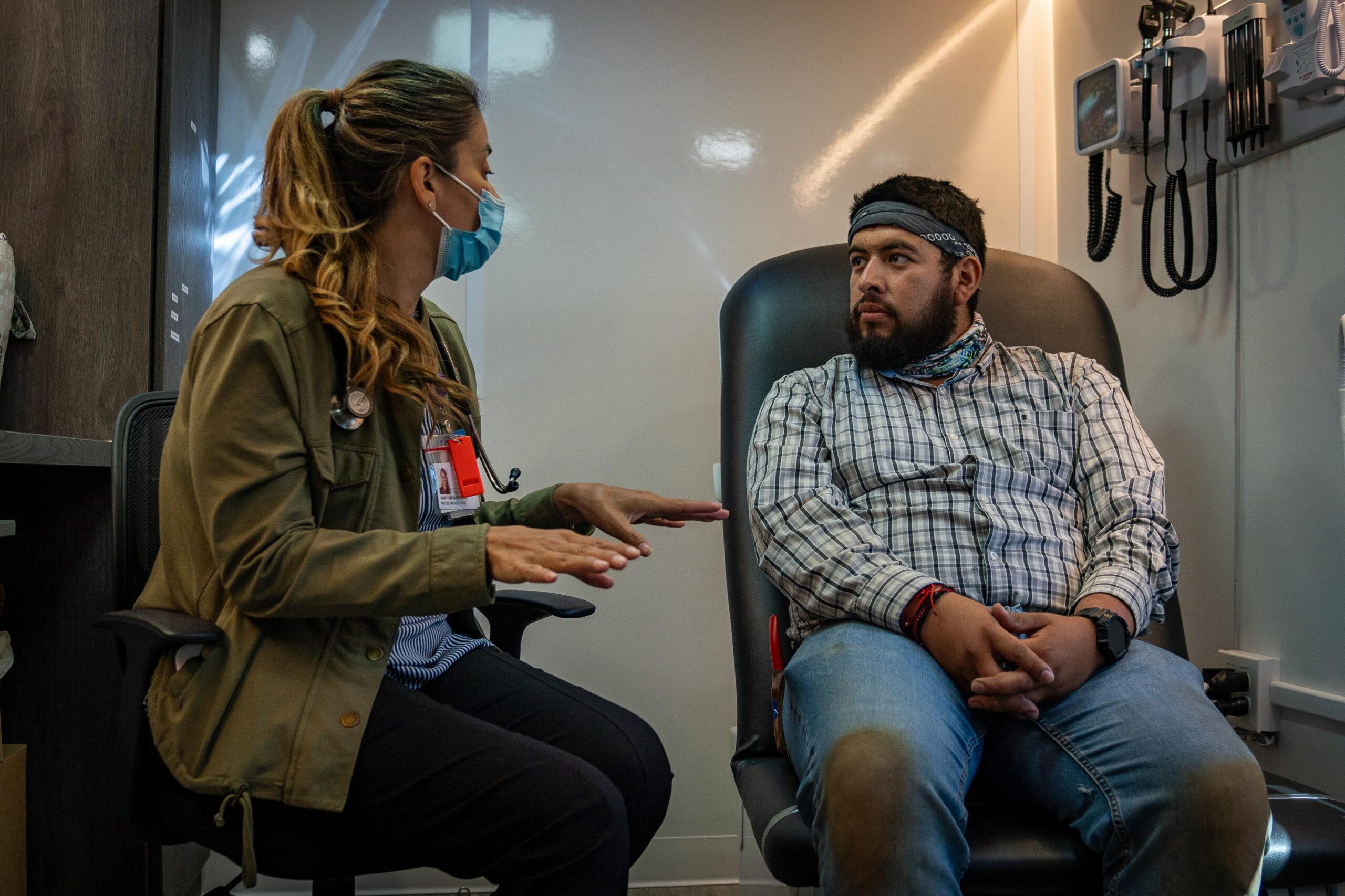 A medical professional wearing a mask talking to a man sitting in a chair