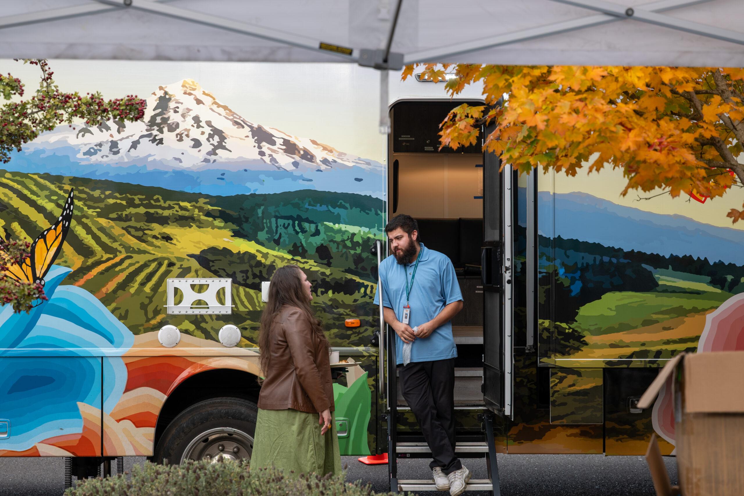 dos miembros del personal de pie y hablando delante de la clínica móvil
