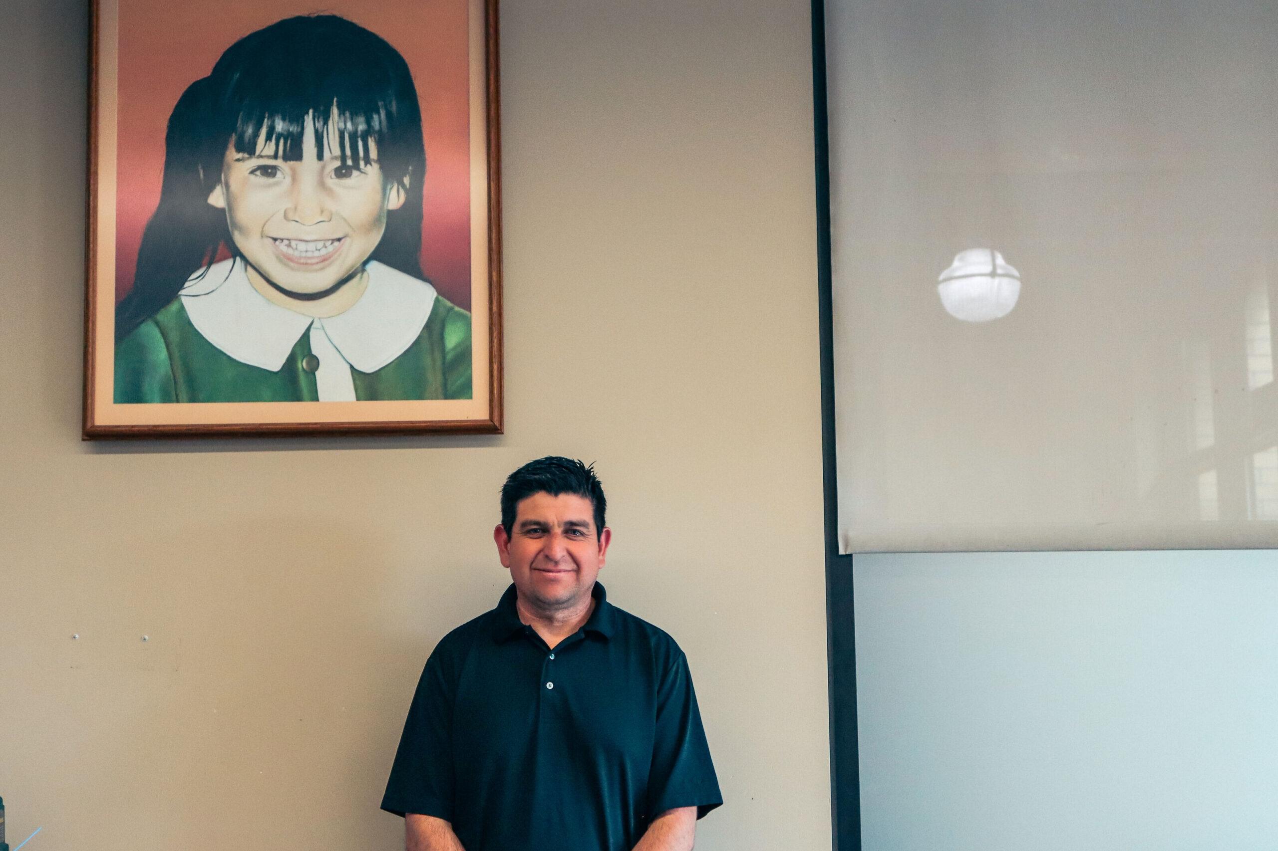 Hombre de pie frente a una pared con una foto de niño detrás de él