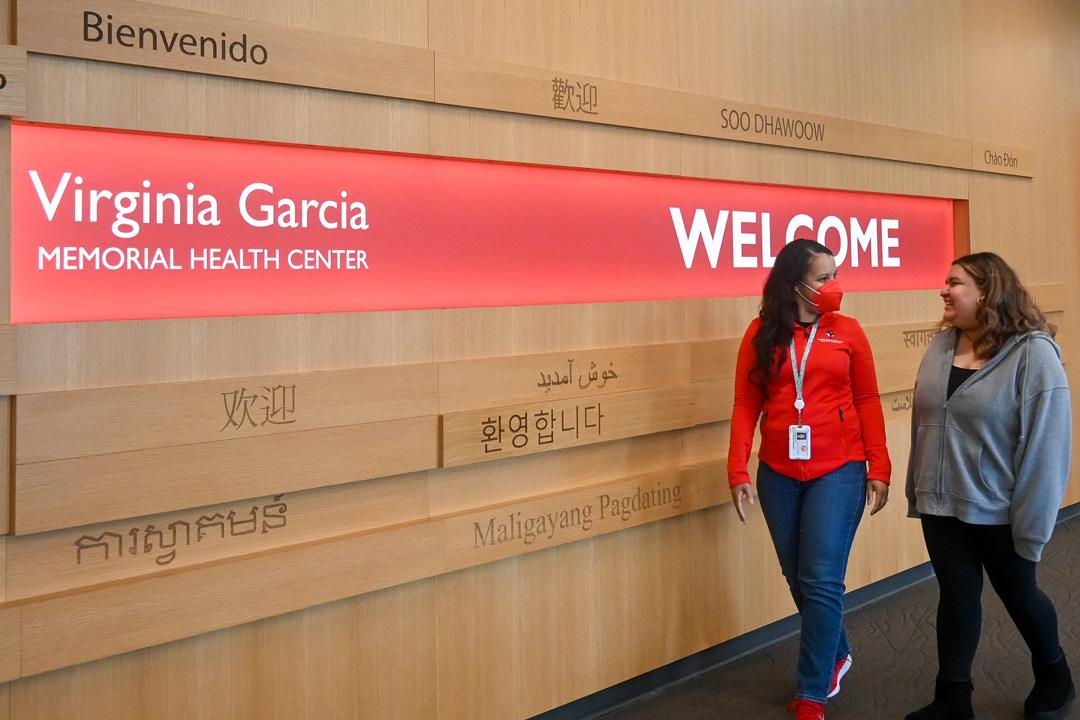 Two women walking in front of the welcome wall inside a virginia garcia building
