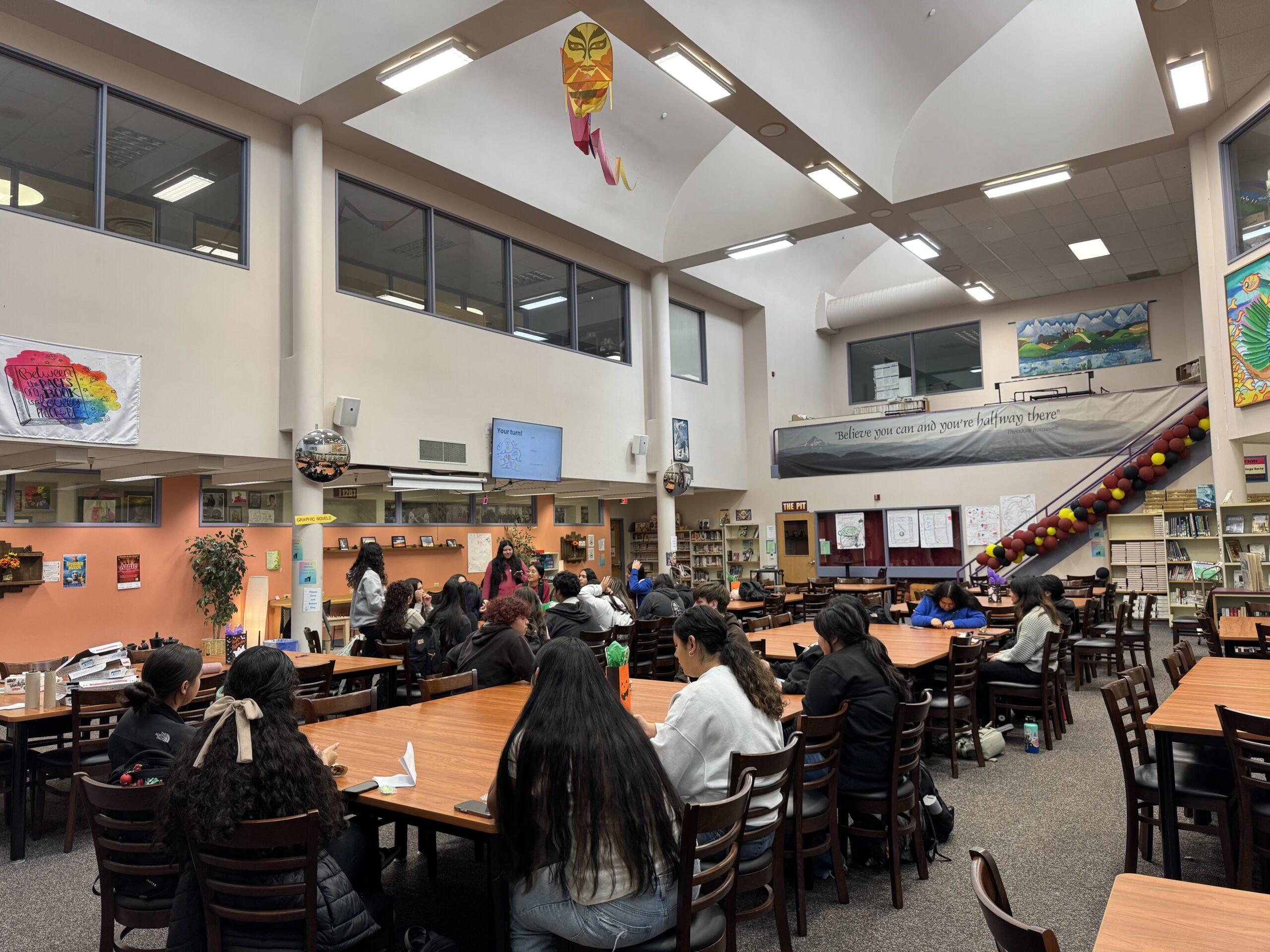 Large group of students gathered around many tables inside a high school