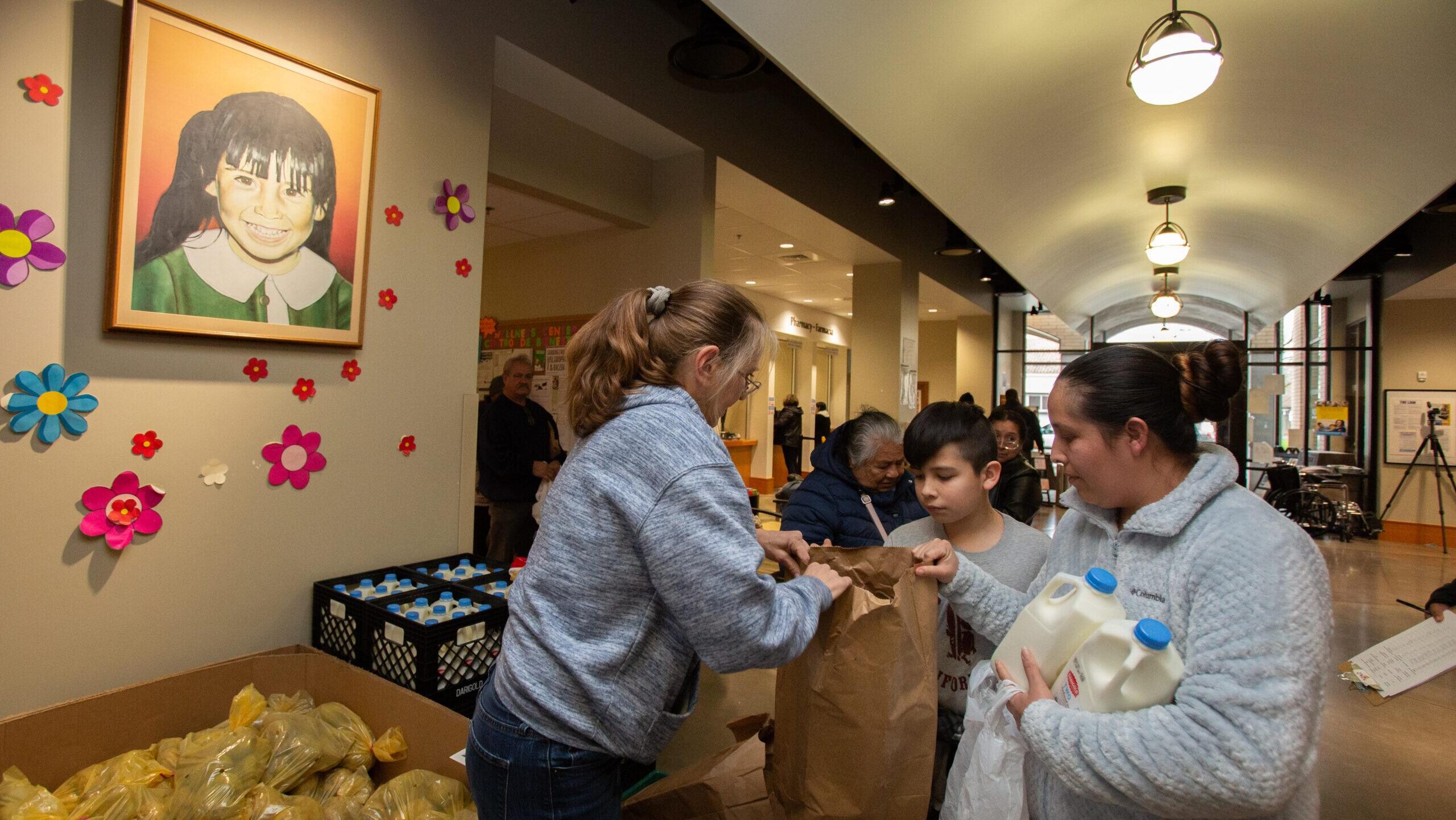 A woman distributes groceries to a mother and child at a community food market.